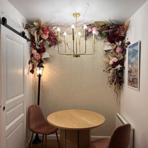 Arche murale de fleurs séchées bordeaux et rose encadrant un coin repas et son lustre doré