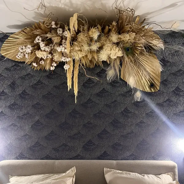 Grande composition de fleurs séchées, épis et plumes de paon au-dessus d'une tête de lit